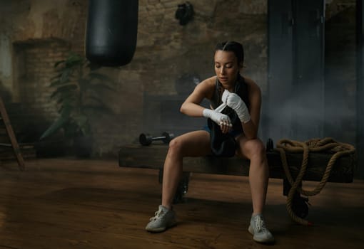 Athletic young female boxer wrapping bandages on her hands preparing to fight in gym