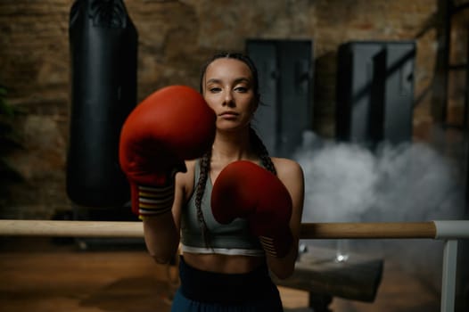 Pretty sportive woman boxer punching with boxing gloves during training headshot portrait. Sport competition preparation, hobby and success concept