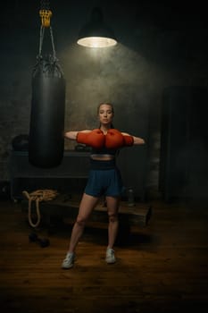 Portrait of professional beautiful sportive woman in red boxing gloves posing in gym studio