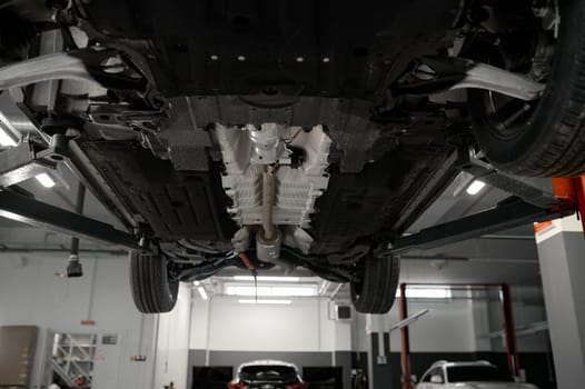 Bottom view of raised car on lift in repair garage. Visible details and structure of suspension or elements of exhaust system