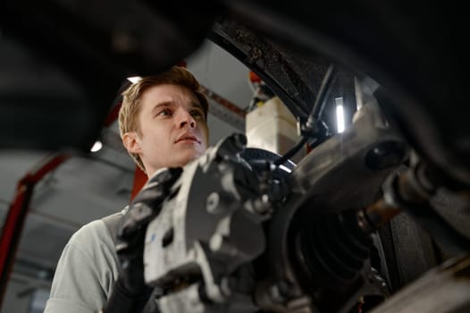 Professional auto mechanic working on car undercarriage view from internal part of vehicle