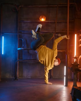 Modern hip hop dancer frozen in movie standing on one hand holding steel pilon tube practicing in dance over urban underground background