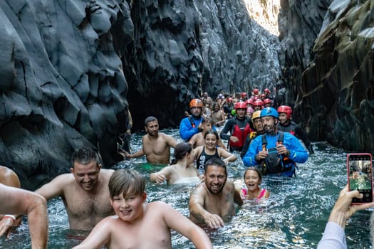 GOLE DI ALCANTARA, SICILY, ITALY - AUGUST 3 2022 diverse group of tourists passing through the cold river between the steep rocks of Gole Alcantara park