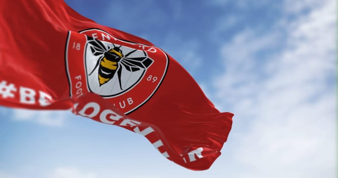 London, UK, Feb 19 2023: Brentford Football Club flag waving in the wind on a clear day. Circular emblem with a bee inside on red. Illustrative editorial 3d illustration render