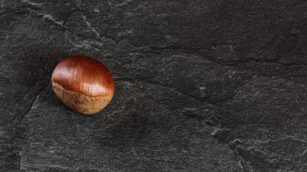 Flat lay photo - detailed close up of chestnut on black stone board.