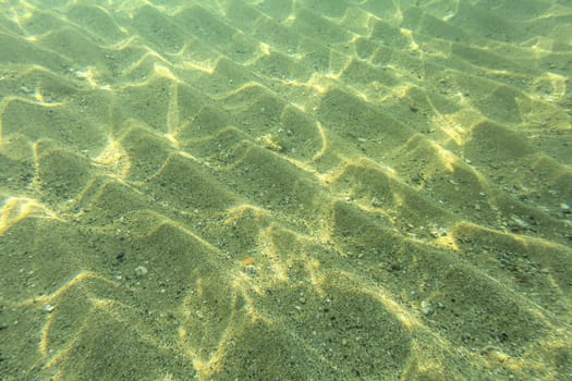 Underwater photo - seafloor, sun shines on sand "dunes"" in shallow sea water near beach, abstract marine background."