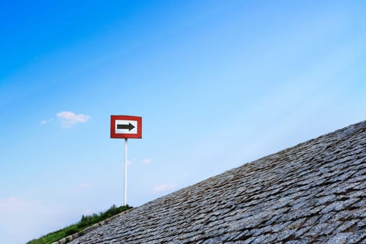 Black arrow on white background and in red frame standing atop of cobblestone paved hill at day. Blue sky with great clouds. Copy space, concept of direction, choice, signal, symbol, hope, options, opportunities, right