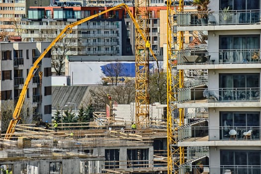 Construction workers install formwork and iron rebars or reinforcing bar for reinforced concrete partitions at the construction site of a large residential building. Pouring concrete from concrete hopper on sunny spring day. Modern cityscape, houses