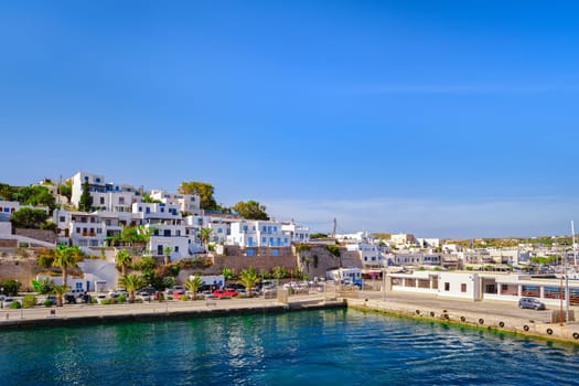 Beautiful summer day and sunshine in typical port town of Greek island. Whitewashed houses on hills and by waterfront. Mediterranean lifestyle, vacations, island hopping, crueses. Milos, Cyclades, Greece.