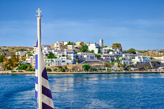 Greek flag and blurred typical Greek island landscape background. Bright summer day. Island hopping, adventures and exploring Mediterranean sea. Selective focus