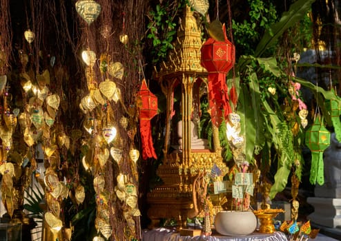 Traditional Thai Buddha altar as busabok with money and incense sticks offerings, colorful Lanna lanterns. Bodhi tree with golden leaves with wishes and promises in many languages. Selective focus, blurred background. Golden Mount, Bangkok, Thailand