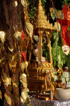Traditional Thai Buddha altar as busabok with money and incense sticks offerings, colorful Lanna lanterns. Bodhi tree with golden leaves with wishes and promises in many languages. Selective focus, blurred background. Golden Mount, Bangkok, Thailand