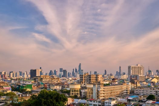 Beautiful cityscape of Bangkok city center in evening, low sun, blue sky and clouds, Thailand. Cheap and abandoned low-rises in foreground, traditional temples, high-rises in downtown with King Power Mahanakhon skyscraper in center.