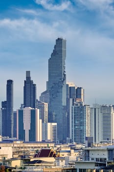 Beautiful cityscape of Bangkok city center in evening, low sun, blue sky and clouds, Thailand. Cheap and abandoned low-rises in foreground, traditional temples, high-rises in downtown with King Power Mahanakhon skyscraper in center. Vertical shot