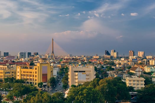 Beautiful cityscape of Bangkok city center in evening, low sun, blue sky and clouds, Thailand. Skyline featuring local landmark of Rama VIII suspension bridge over Chao Praya river and residential area.