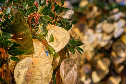 Traditional form of prayer in Thailand, artificial golden leaves with handwritten wishes in many languages tied to Bodhi tree branches. Selective focus, blurred background. Religion, rituals, worship, wishes, multi-language.