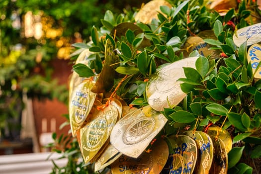Traditional form of prayer in Thailand, artificial golden leaves with handwritten wishes in many languages tied to Bodhi tree branches. Selective focus, blurred background. Religion, rituals, worship, wishes, multi-language.