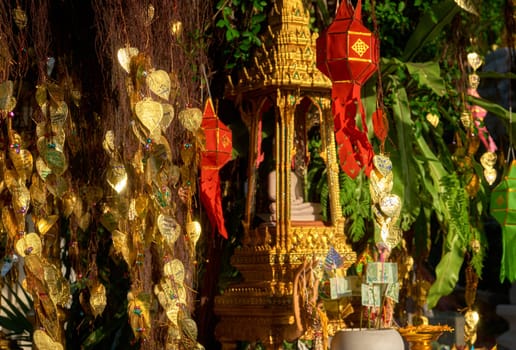 Traditional Thai Buddha altar as busabok with money and incense sticks offerings, colorful Lanna lanterns. Bodhi tree with golden leaves with wishes and promises in many languages. Selective focus, blurred background. Golden Mount, Bangkok, Thailand