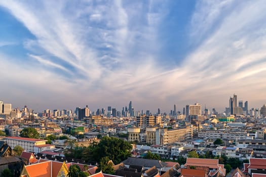 Beautiful cityscape of Bangkok city center in evening, low sun, blue sky and clouds, Thailand. Residential low-rises and traditional Buddhist temples in foregrounds, high-rises in downtown with King Power Mahanakhon skyscraper in distance. Colorful urbanscape