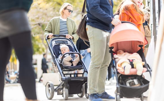 Mother walking and pushing his infant baby boy child in stroller in crowd of people wisiting sunday flea market in Malaga, Spain