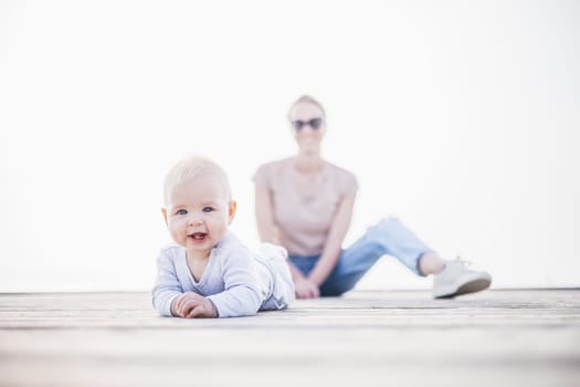 Happy family. Young mother playing with her baby boy infant oudoors on sunny autumn day. Portrait of mom and little son on wooden platform by lake. Positive human emotions, feelings, joy