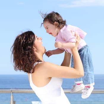 Pretty mum laughing and raising her baby girl with the sea in the background