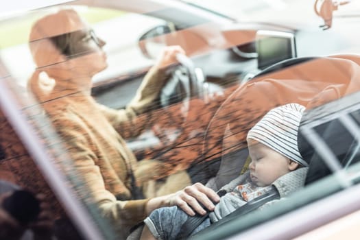 Mother concentrating on driving family car running errands while her baby sleeps in infant car seat by her site