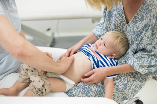 Infant baby boy child being examined by his pediatrician doctor during a standard medical checkup in presence and comfort of his mother. National public health and childs care care koncept