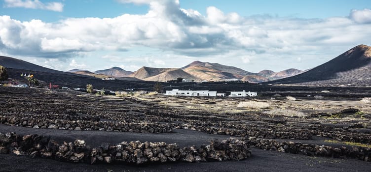 Traditional white houses in black volcanic landscape of La Geria wine growing region with view of Timanfaya National Park in Lanzarote. Touristic attraction in Lanzarote island, Canary Islands, Spain