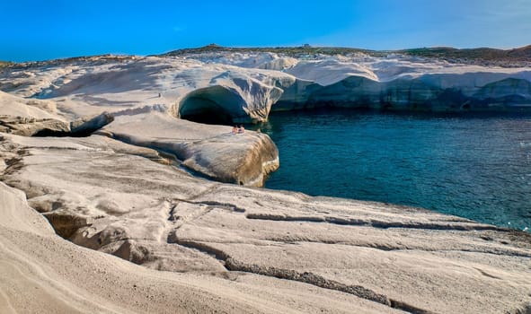 Beautiful landscape of white rocks, Sarakiniko beach, Aegean sea, Milos island, Greece. Empty cliffs, summer day sunshine, clear sea, blue waters, azure lagoon, two unrecognizable adults, beautiful landscape, fantastic rocks of tourist destination.