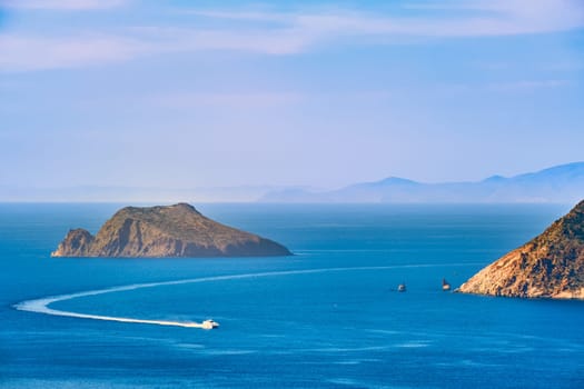Beautiful landscape with several islets in bay, distant hazy shores, blue sea waters, great sky, sunny summer day in Mediterranean sea. Small ferry speedboat enter picturesque harbour, perfect Greek travel and vacation. Milos island, Greece.
