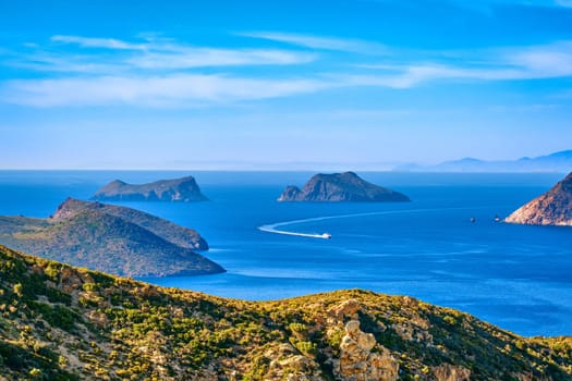 Beautiful landscape with several islets in bay, distant hazy shores, blue sea waters, great sky, sunny summer day in Mediterranean sea. Small ferry speedboat enter picturesque harbour, perfect Greek travel and vacation. Milos island, Greece.