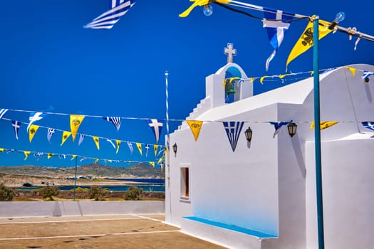 White Greek Orthodox chapel or church on top of hill decorated Greek national, Greek Orthodox flag. Traditional religious building, clear blue sky on sunny summer day. Typical Greek landscape, island, Mediterranean sea. Milos Greece
