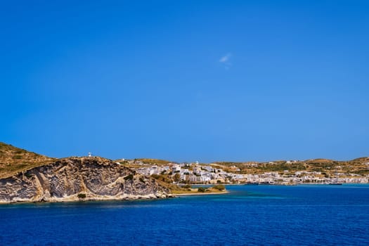 Beautiful summer day and sunshine in typical port town of Greek island. Whitewashed houses on hills and by waterfront. Mediterranean lifestyle, vacations, island hopping, crueses. Milos, Cyclades, Greece.