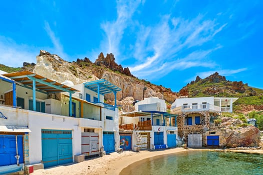 Traditional Greek fishing village of Firopotamos, Milos island, Cyclades, Greece. Colorful boat house doors, whitewashed houses, high cliffs, blue sky, azure sea waters, no people by waterfront, summer day sunshine.