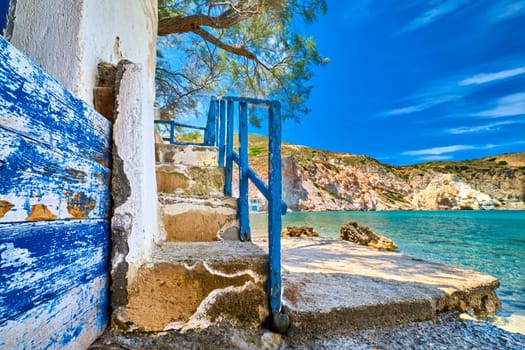Weathered stairway to azure sea waters of secluded bay on Greek island. Whitewashed walls and concrete steps in rocky cliff washed by waves. Typical Greek summer landscape of harbour on island, sunny summer day. Perfect vacations location.