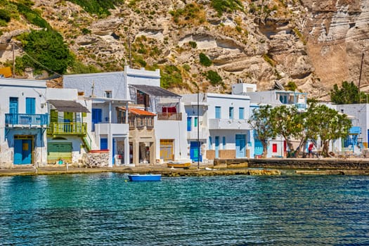 Close view of colorful village of Klima with Greek whitewashed houses on sunny day, Milos island, Cyclades, Greece. Traditional fishermen village, bright painted and weathered doors and doorways, high hill, azure sea, summer sunshine, vacations.