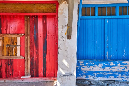 Colorful blue and red boat garage doors in Klima fishermen village, Milos island, Greece. Traditional whitewashed house walls, painted, faded and weathered wooden doors and doorways, sunny summer day, authentic architecture and details. Frontal shot