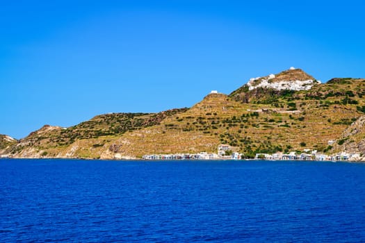 Beautiful summer day and sunshine in typical hill top town of a Greek island. Whitewashed houses on hills and by waterfront. Mediterranean lifestyle, vacations, island hopping, crueses. Milos, Cyclades, Greece.