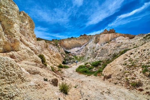 Lonely male adult explore majestic rocks of Greek island landscape. Sunny summer day. beautiful sky, little greenery, limestone cliffs. Nature, outdoor activities, hiking, mountains. Firopotamos beach, Milos island, Greece.