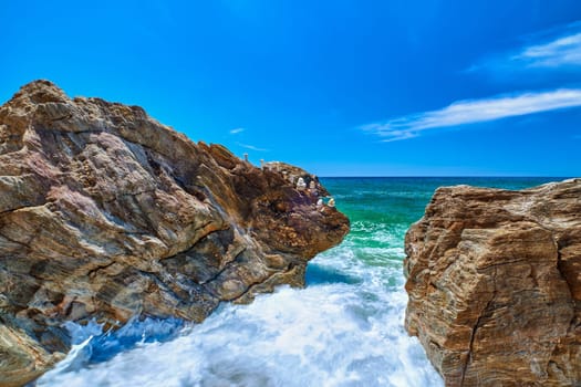 Sea waves beat in rocks on sunny summer day, clear sky, long exposure. Tiny balance stone stack on edge of rock. Azure waters, white sea spray. Perfect seascape, vacations destination. Paleochori beach, Milos, Greece