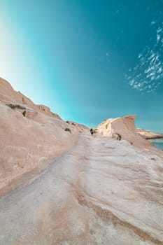 Beautiful white rocks of Sarakiniko beach, Aegean sea, Milos island , Greece. Lonely unrecognizable adult, empty cliffs, summer day sunshine, lunar landscape, fantastic rocks of tourist destination, sky, clouds, cyan-pink colors, vertical shot