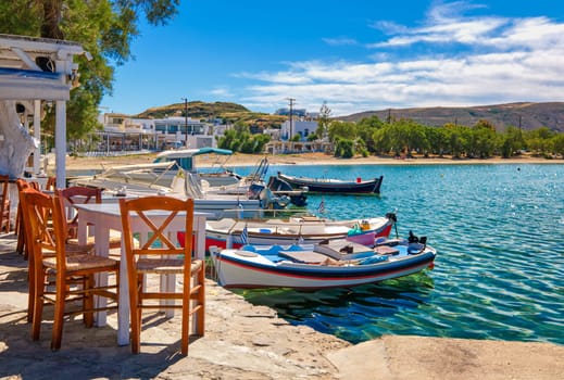 Colorful chairs and tables of Greek tavern by waterfront at sunny day. Vacations in Greece, summer, restaurant, outdoor dining, port, marina, yachts and boats, Mediterranean relax, Cyclades and Aegean islands. Selective focus, blurred background.