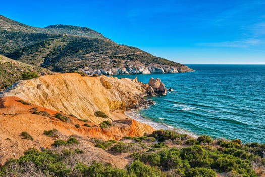 Beautiful sunset view of secluded and remote beach on sunny evening. High yellow cliffs, weathered rocks, azure sea waters, sandy beach, clear sky, no people. Agios Ioannis beach and Aegean sea, Milos island, Greece.