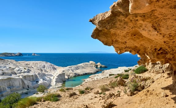 Famous white rocks of Sarakiniko beach, Aegean sea, Milos island , Greece. Empty cliffs, summer day sunshine, clear sea, blue waters, azure lagoon, big orange rock, one adult goes swimming, beautiful landscape, fantastic tourist destination.