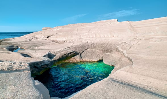 Beautiful white rocks and emerald green water in sea cave Sarakiniko beach, Aegean sea, Milos island , Greece. Empty cliffs, summer day sunshine, no people, lunar landscape, emerald green clear waters, sea cave, fantastic rocks, tourist destination.