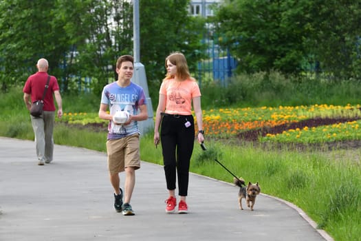 Moscow, Russia - 16 June 2020. Two teenagers walk the Yorkshire terrier on a leash in park