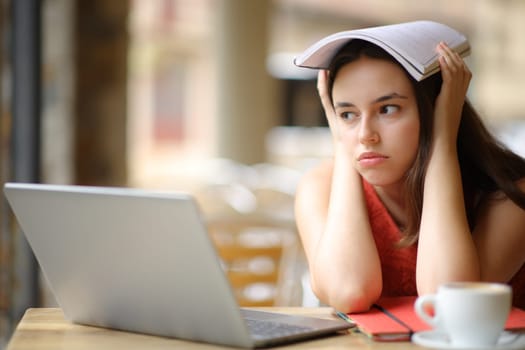 Frustrated student distracting looking away sitting in a bar terrace
