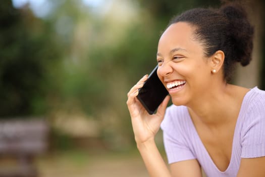 Happy black woman talking on phone laughing in a park