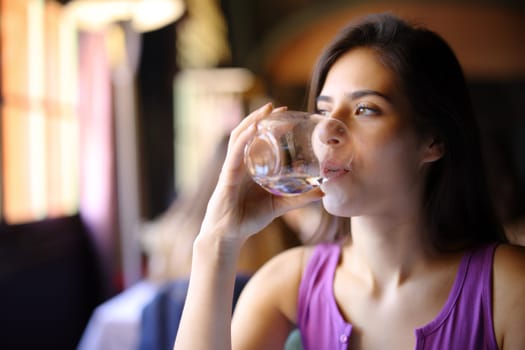 Woman drinking water from glass sitting in a restaurant interior